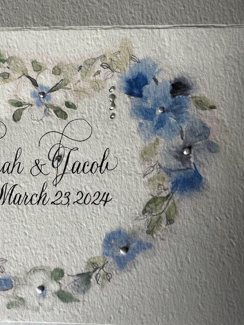 Puede incluir: Una invitaci&oacute;n de boda con un dise&ntilde;o floral de acuarela en tonos azules y verdes. La invitaci&oacute;n dice "Sarah & Jacob" y "March 23, 2024".