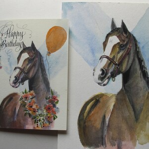 May include: A watercolor painting of a brown horse with a white blaze on its face. The horse is wearing a brown halter and has a floral garland around its neck. The painting is on a white background with a blue sky in the background. The painting says "Happy Birthday" in cursive.