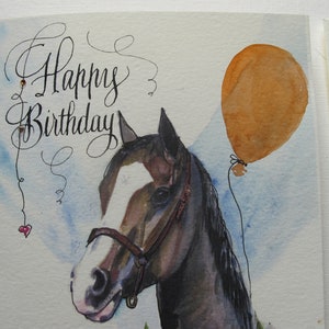 May include: A watercolor painting of a brown and white horse with a black halter. The horse is looking to the left. There is a brown balloon with a string attached to it in the upper right corner of the image. The words "Happy Birthday" are written in cursive in the upper left corner of the image.