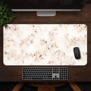 May include: A rectangular desk mat with a floral design in shades of beige and brown. A black computer mouse rests on the mat, near a black keyboard. The mat features a watercolor-style pattern of flowers and leaves.