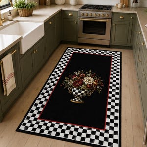 May include: A rectangular area rug featuring a black center with a red border and a black and white checkered pattern along the edges. The center displays a decorative urn filled with a colorful floral arrangement of red, white, and green flowers.