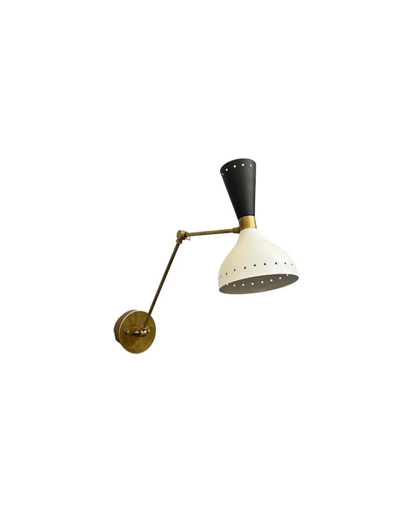 May include: A black and white wall sconce with a brass arm and a white shade with holes. The sconce is adjustable and can be tilted up or down.