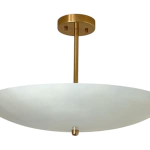May include: A modern ceiling light fixture with a white, oval-shaped shade. The fixture has a gold-colored stem and a circular ceiling mount. The light is suspended from the ceiling, providing ambient illumination.