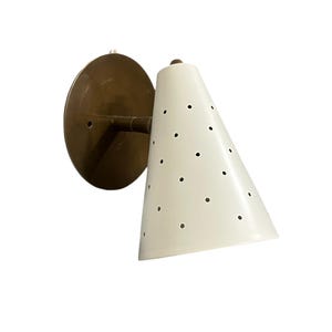 Könnte beinhalten: Eine weiße, konische Wandleuchte mit Messingsockel und perforiertem Design. Die Leuchte ist an einer weißen Wand montiert.