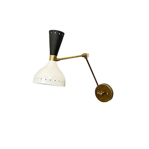 May include: A black and white wall sconce with a brass arm and a round base. The sconce has a white shade with holes and a black top.