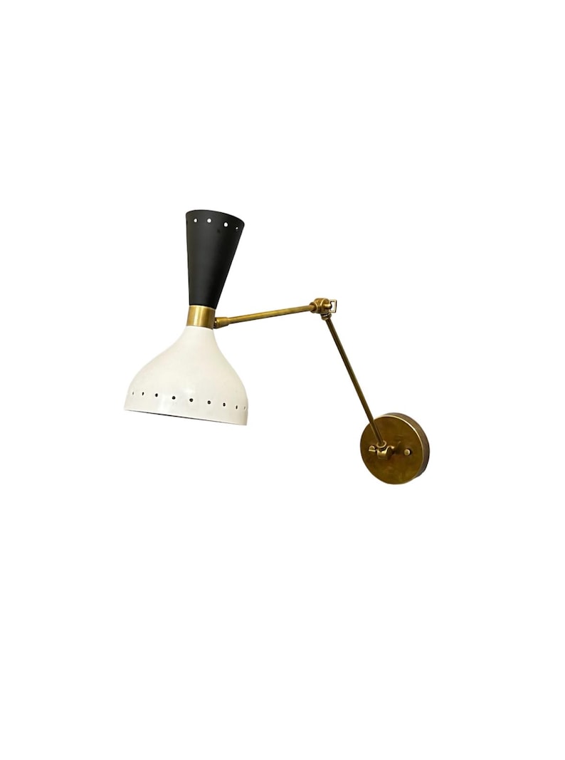 May include: A black and white wall sconce with a brass arm and a round base. The sconce has a white shade with holes and a black top.