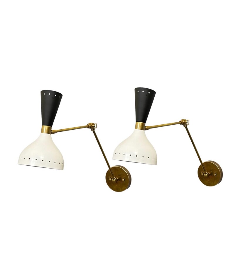 May include: A pair of black and white wall sconces with brass arms. The sconces have a white, perforated shade and a black, cone-shaped top.
