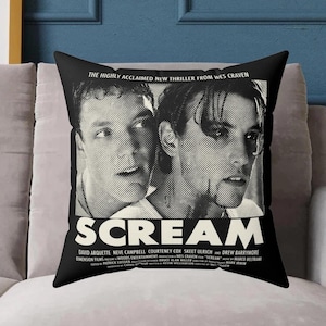 Puede incluir: Una almohada de color negro y blanco con un póster de la película "Scream" con los actores David Arquette y Neve Campbell. El texto en la almohada dice "The Highly Acclaimed New Thriller From Wes Craven" y "Scream".