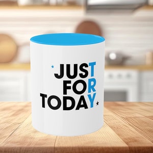 May include: White ceramic mug with a blue rim. The mug has black text that reads "*JUST TRY FOR TODAY*" with a star on either side of the text.