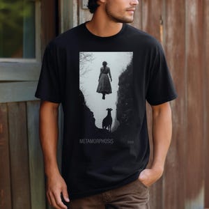 May include: Black t-shirt with a graphic print of a woman floating in the air with a goat below her. The text "METAMORPHOSIS" is printed below the graphic.