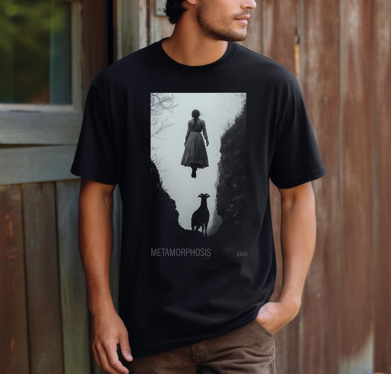 May include: Black t-shirt with a graphic print of a woman floating in the air with a goat below her. The text "METAMORPHOSIS" is printed below the graphic.