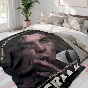 May include: Black and white movie poster throw blanket featuring a close-up of a man's face with blood on his mouth. The text "The Highly Acclaimed New Thriller From..." is visible at the top left corner of the blanket. The text "...Neve Campbell,  ...Urteiney Cox, Skeet Ulrich and ...Drew Barrymore" is visible at the bottom of the blanket. The title of the movie is "Scream".