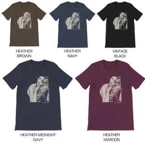 May include: Five t-shirts in different colors featuring a black and white image of a woman with her head resting on a tree branch. The image is printed on the front of the shirts. The colors of the shirts are heather brown, heather navy, vintage black, heather midnight navy, and heather maroon.