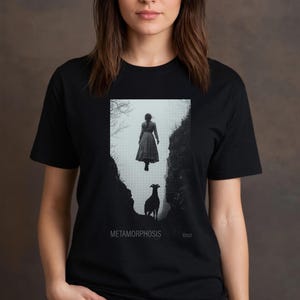 May include: Black and white graphic t-shirt featuring a woman floating in the air above a goat in a canyon. The text "METAMORPHOSIS" and "XXVII" are printed on the shirt.