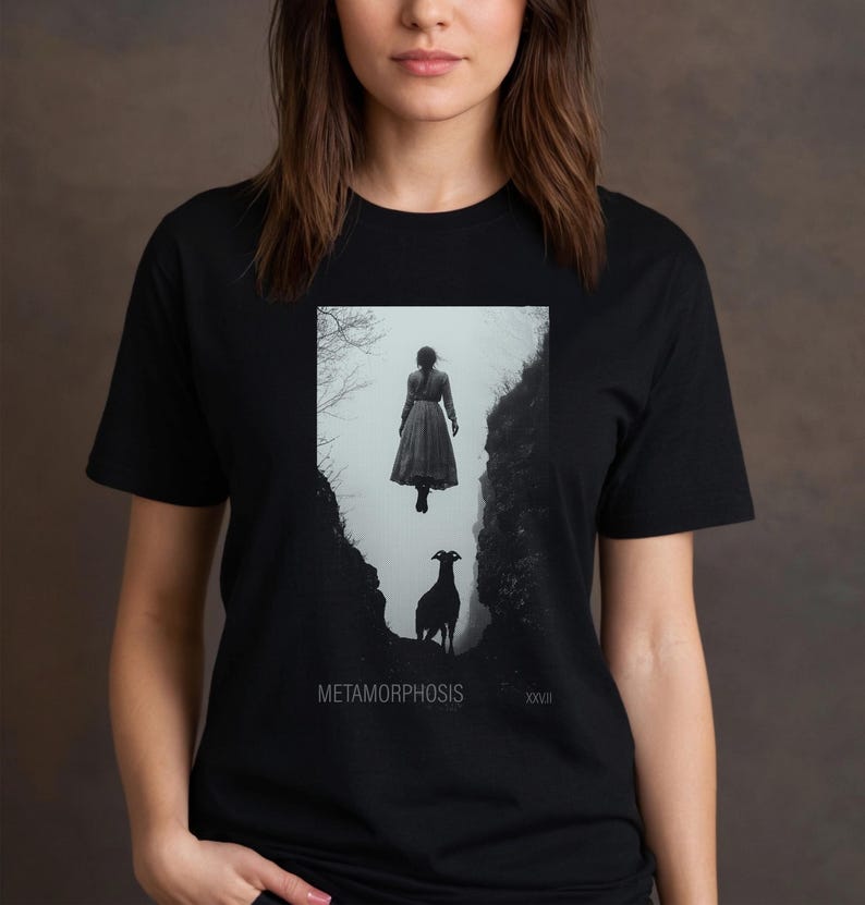 May include: Black and white graphic t-shirt featuring a woman floating in the air above a goat in a canyon. The text "METAMORPHOSIS" and "XXVII" are printed on the shirt.