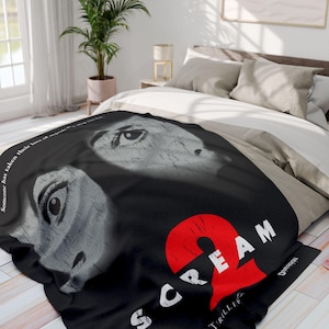 May include: Black and white throw blanket with a Scream 2 movie poster design. The poster features a red number 2 and the words "Scream 2" in white. The poster also features two black and white images of a woman's face with a large eye.