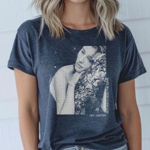 May include: A dark blue t-shirt with a graphic print of a woman with her head resting on a tree branch. The text "HEY JUPITER" and "NOTHING'S BEEN THE SAME" are printed on the shirt.