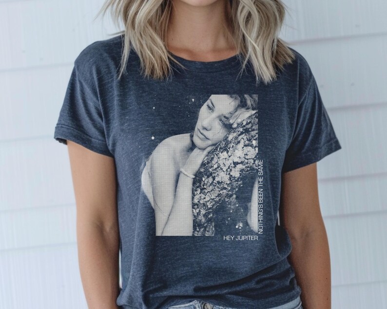 May include: A dark blue t-shirt with a graphic print of a woman with her head resting on a tree branch. The text "HEY JUPITER" and "NOTHING'S BEEN THE SAME" are printed on the shirt.