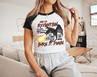 May include: A white t-shirt with black sleeves featuring a black dragon with red flames. The text "JOIN THE REVOLUTION" is printed on the shirt, along with the names of various performers and the phrase "BURN. IT. DOWN."