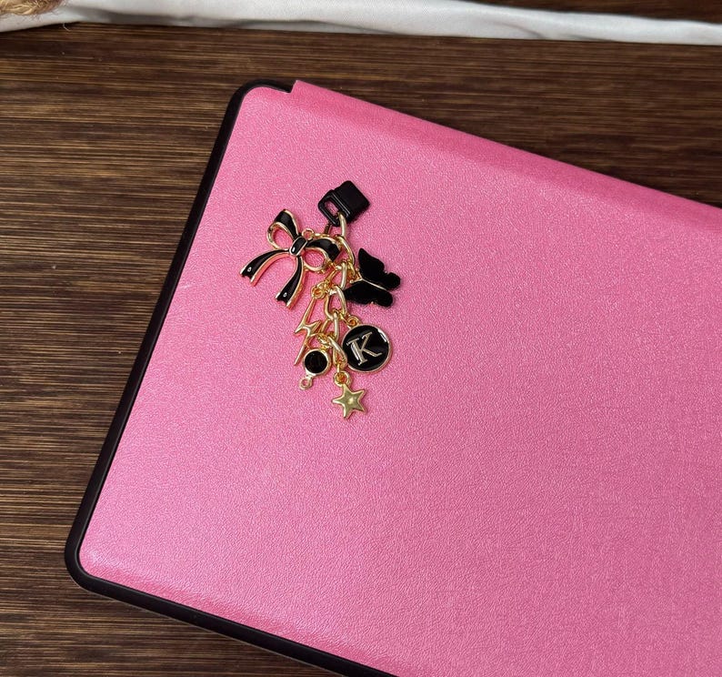 Op de afbeelding: Een roze leren notitieboekje met een gouden bedel eraan. De bedel heeft een zwarte strik, een gouden ster en een gouden letter 'K'.