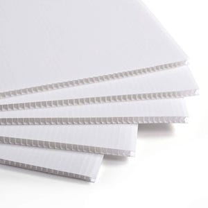 May include: A pile of white corrugated plastic sheets. The sheets are layered, showing the fluted internal structure. The edges are neat and the material looks new. The image is well-lit, highlighting the texture and form of the plastic.