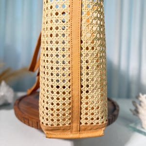 A woven basket with a tan-colored interior and a brown handle, placed on a wooden surface against a blue background.