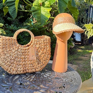 a woven straw handbag and a straw hat placed on a metal table, surrounded by potted plants and greenery.