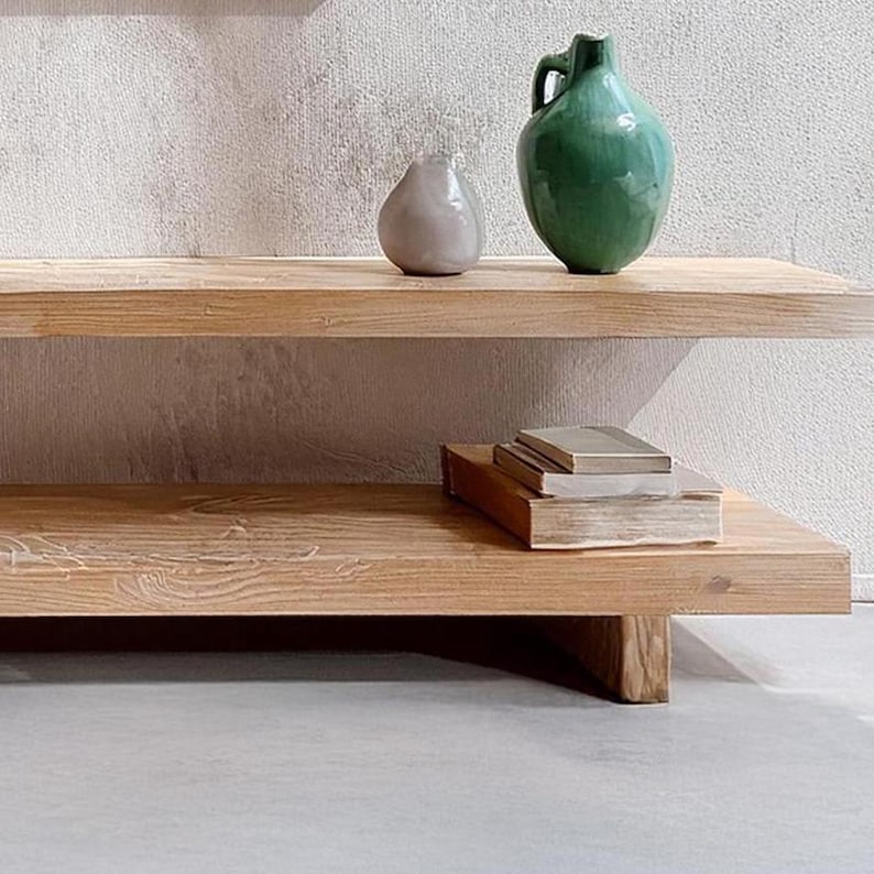 May include: A two-tiered wooden shelf with a light wood finish. The top shelf has a green ceramic pitcher and a gray ceramic pear. The bottom shelf has a stack of books.