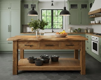 May include: A rustic wooden kitchen island with three drawers and a lower shelf, holding several black pots. The island is topped with a live-edge wooden surface. The kitchen features sage green cabinets, a white brick backsplash, and black pendant lights.