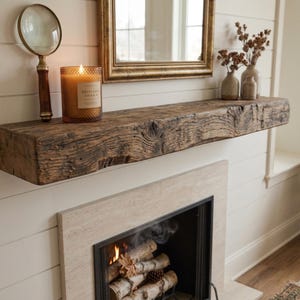May include: A thick, rectangular wooden mantelpiece with a dark, weathered finish and visible wood grain texture. The mantel is mounted above a fireplace and holds a magnifying glass with a wooden handle and a lit candle in a textured glass jar.