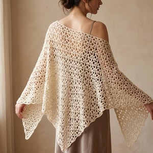 May include: A cream-coloured, open-weave crochet shawl. The shawl is draped over the shoulders, with the open weave design creating a delicate, airy look. The shawl's edges are slightly scalloped, adding a touch of elegance. A versatile accessory for layering.
