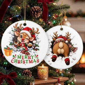 Op de afbeelding: Twee ronde witte keramische ornamenten met een cartoon rendier. Het linker ornament toont het knipogende rendiergezicht met een rode muts en sjaal, met de tekst Merry Christmas. Het rechter ornament toont de achterkant van het rendier.