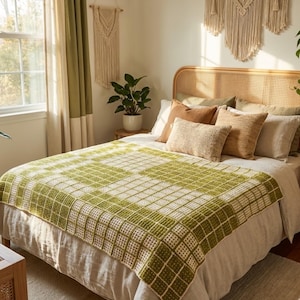 May include: A bed with a woven headboard and a green and white checkered blanket. The bed is made with several pillows in shades of brown and beige. A potted plant and macrame wall hangings add to the room's decor.