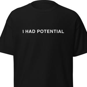 Könnte beinhalten: Schwarzes T-Shirt mit dem weißen Text "I HAD POTENTIAL" auf der Brust. Das Shirt hat kurze Ärmel und einen Rundhalsausschnitt. Der Stoff scheint ein weiches, bequemes Material zu sein.