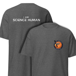 May include: Two charcoal gray t-shirts. The front shirt has a small circular patch with the text "HAIL MARY EARTH" and a rocket ship design. The back shirt has the text "I AM SCIENCE HUMAN".