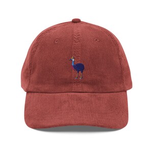 May include: A red corduroy baseball cap with an embroidered image of a cassowary bird.