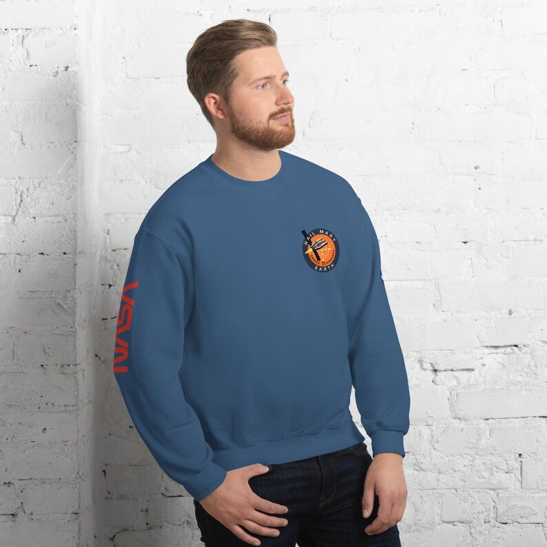May include: A blue sweatshirt with the word "NASA" printed vertically in red on the left sleeve. The right chest features a circular patch with a graphic of a rocket and the words "ALL MARS EARTH".