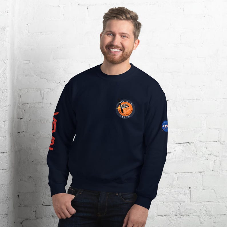 May include: Navy blue sweatshirt with the NASA logo on the right sleeve and a circular patch on the chest that reads "Hail Mary Earth". The left sleeve has the word "NASA" in orange. The sweatshirt is a crew neck style.