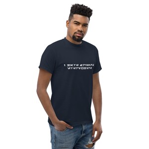 May include: Navy blue t-shirt with white text in an alien language. The t-shirt is a classic crew neck style. The model is wearing blue jeans.
