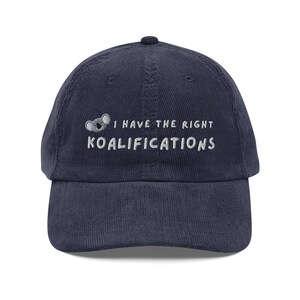 May include: A navy blue corduroy baseball cap with white embroidered text that reads "I have the right koalifications" and a small koala bear graphic.