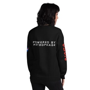 May include: Black sweatshirt with the text "POWERED BY ASTROPHAGE" in white on the back. The NASA logo is on the left sleeve, and the word "NASA" is printed in red on the right sleeve. A casual, comfortable garment.