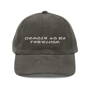 May include: Olive green corduroy baseball cap with white embroidered text. The cap has a curved brim and an adjustable strap. The text appears to be in a stylized font. A casual accessory for everyday wear.