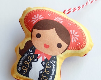 May include: A yellow and red fabric ornament shaped like a person wearing a red and white hat with flowers. The person has brown hair, brown eyes, and a red mouth. The ornament has a white string attached to the top.