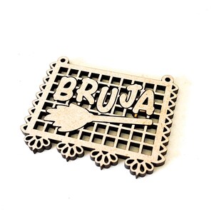 May include: A wooden cutout of a witch with the word "BRUJA" written in Spanish. The cutout is decorated with a grid pattern and a broom.