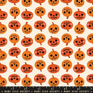May include: A fabric print featuring a repeating pattern of orange jack-o'-lanterns with black facial features and pink cheeks on a cream background, with a black ruler edge at the bottom labeled Ruby Star Society with markings up to 7 inches.