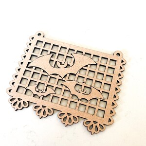 Peut inclure: Une découpe en bois d'une bannière avec un motif de grille et trois chauves-souris. La bannière a un bord festonné et des détails décoratifs en bas.