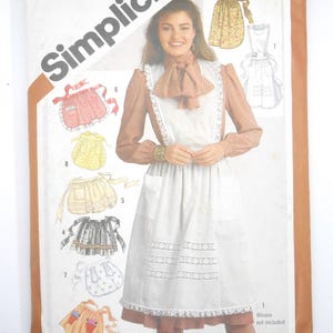 May include: Simplicity sewing pattern featuring various apron designs. The cover displays a woman wearing an apron with a white bib and a ruffled hem. The pattern includes multiple apron styles, with illustrations of each design. The text "ONE SIZE" is visible.