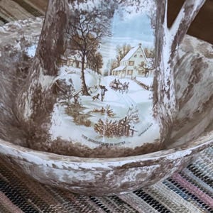 May include: A ceramic wash basin and pitcher set featuring a brown and white mottled finish. The pitcher displays a Currier & Ives winter scene titled The Homestead in Winter, depicting a house, a horse-drawn carriage, and a person with a dog.