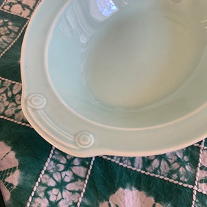 May include: A light blue ceramic bowl with two handles. The bowl has a smooth, glossy finish.