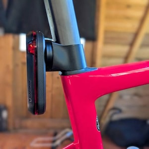 Op de afbeelding: Een zwart Garmin fietsachterlicht bevestigd aan een rood fietsframe. Het licht heeft een rode lens en het Garmin-logo. Het fietsframe heeft een felrode kleur.